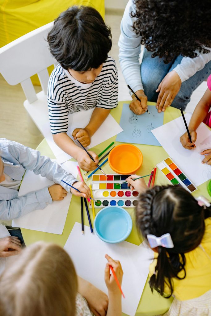 Draufsicht auf Kinder, die im Kunstunterricht im Vorschulalter mit Wasserfarben malen.